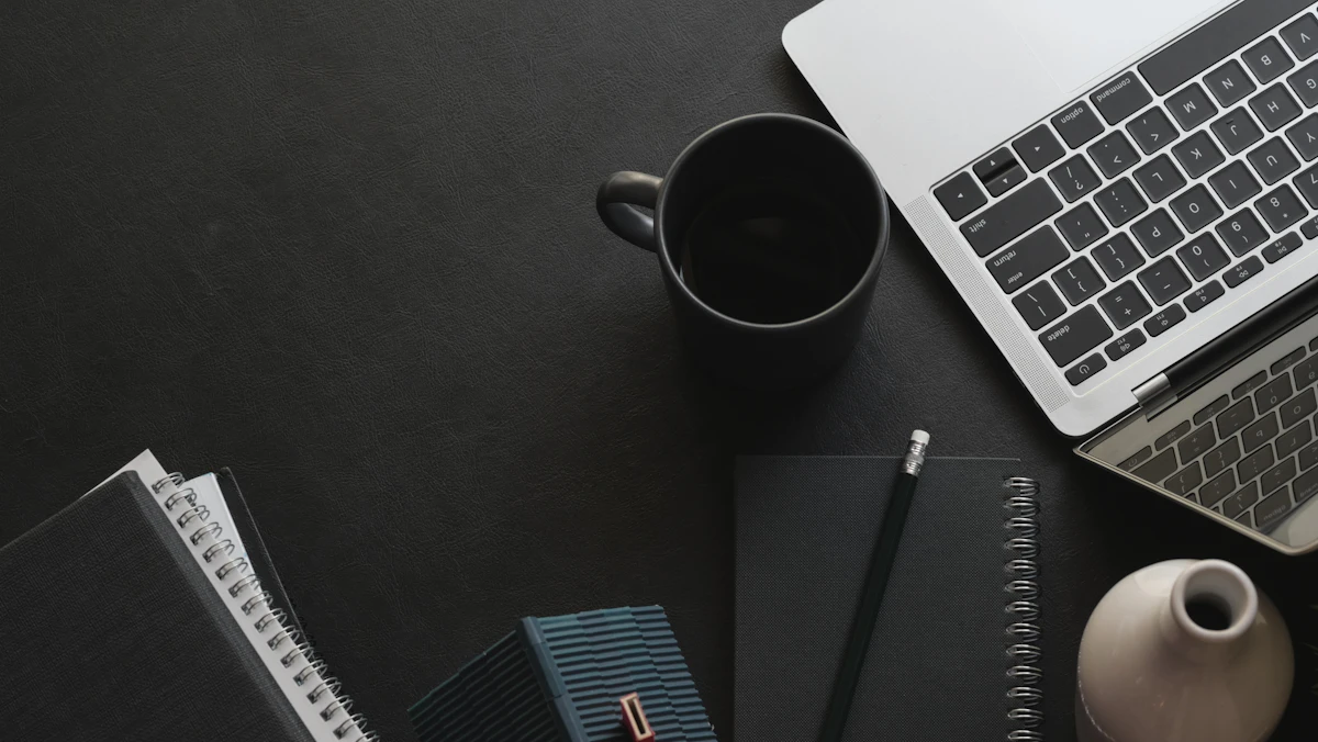 Laptop, coffee cup and notebooks arranged on a dark desk